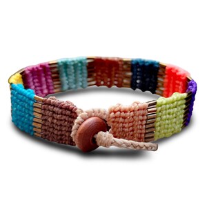 Peut inclure: Bracelet en macramé multicolore avec fermoir en bois. Le bracelet est composé de fils tissés dans des tons de bleu, rose, vert et rouge. Il présente un aspect fait main et une esthétique naturelle.