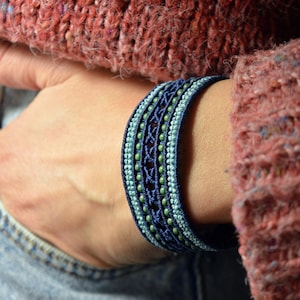 Puede incluir: Un brazalete de cuentas azules y verdes con un diseño tejido. El brazalete se lleva en la muñeca.