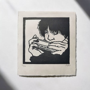 Può includere: Stampa in bianco e nero di una persona che suona l'armonica. La stampa è numerata 2/20.