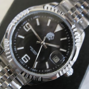 May include: A silver wristwatch with a black face and silver hands. The watch has a date window at the 3 o'clock position and a silver band.