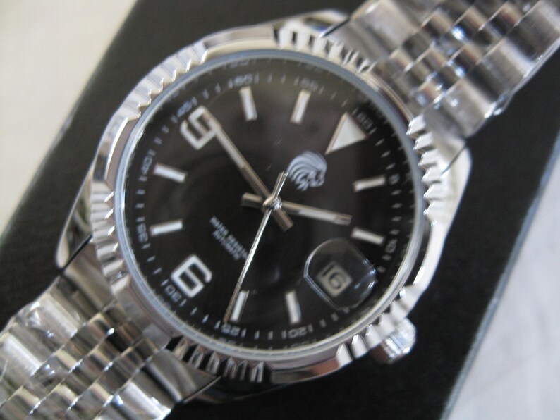 May include: A silver wristwatch with a black face and silver hands. The watch has a date window at the 3 o'clock position and a silver band.