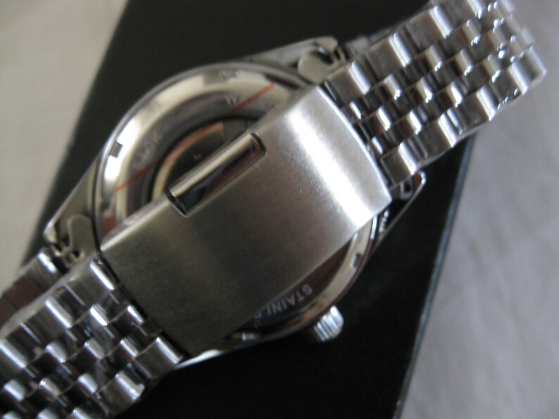 May include: A silver wristwatch with a stainless steel band. The watch face is silver with black markings. The watch has a silver clasp.