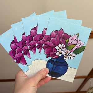 Puede incluir: Cinco tarjetas con una pintura de flores rosas y blancas en un jarrón azul sobre un fondo azul claro.