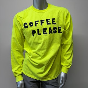 Puede incluir: Una camiseta de manga larga de color amarillo brillante con el texto "COFFEE PLEASE" impreso en negro.