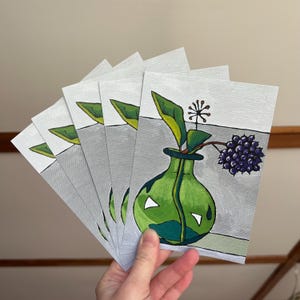 Puede incluir: Cinco postales pintadas en verde y blanco con un jarrón verde con un solo tallo verde y bayas moradas. El jarrón está sobre un fondo blanco.