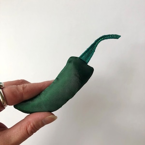 May include: A dark green fabric pepper shaped pillow with a green fabric stem.