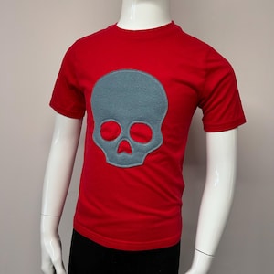 Puede incluir: Camiseta roja de manga corta con un diseño de calavera gris.