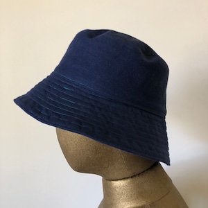 Puede incluir: Un sombrero de cubo azul marino con un borde azul oscuro y un detalle de costura verde sutil.