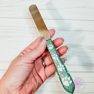 May include: A green and gold glitter spatula with white paw prints. The spatula has a stainless steel blade.