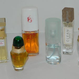 Puede incluir: Una colecci&oacute;n de frascos de perfume de varias formas y tama&ntilde;os. Los frascos contienen l&iacute;quidos de diferentes colores, incluyendo amarillo, naranja y azul. Algunos frascos tienen etiquetas y otros tienen tapones decorativos. Los frascos est&aacute;n dispuestos sobre una superficie blanca.