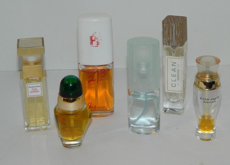 Puede incluir: Una colecci&oacute;n de frascos de perfume de varias formas y tama&ntilde;os. Los frascos contienen l&iacute;quidos de diferentes colores, incluyendo amarillo, naranja y azul. Algunos frascos tienen etiquetas y otros tienen tapones decorativos. Los frascos est&aacute;n dispuestos sobre una superficie blanca.