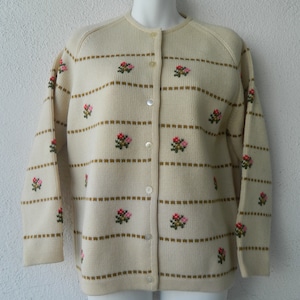 May include: A cream-colored cardigan with brown stripes and embroidered floral designs. The cardigan has a button-up front and long sleeves.