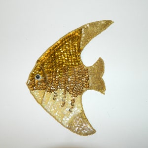 May include: A gold and white sequined fish applique. The fish is shaped like an angelfish and has a large, rounded body and a long, flowing tail.