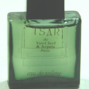 May include: A green glass bottle of Tsar de Van Cleef & Arpels eau de toilette. The bottle is rectangular with a black square cap. The text "TSAR" and "eau de toilette" are visible on the front.