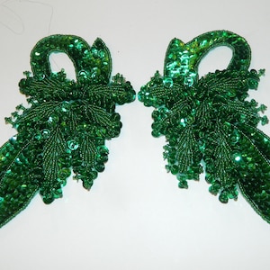 May include: Two green sequined embellishments with a leaf design. The embellishments are made of green sequins and beads.