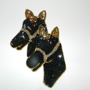 May include: Two black horse head appliques with gold and silver sequins and beads. The horse heads are facing forward and are layered on top of each other.