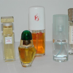 Puede incluir: Una colecci&oacute;n de frascos de perfume de varias formas y tama&ntilde;os. Los frascos contienen l&iacute;quidos de diferentes colores, incluyendo amarillo y naranja. Un frasco tiene una tapa dorada y una etiqueta que dice "5th avenue". Otro frasco tiene una tapa verde.