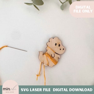 May include: A wooden dinosaur cutout with a yellow thread wrapped around it. The dinosaur is on a white surface with a needle and thread nearby. The text "SVG LASER FILE DIGITAL DOWNLOAD" is at the bottom of the image.