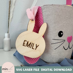 May include: A wooden bunny-shaped tag with the name "Emily" engraved on it. The tag is attached to a pink and white polka dot fabric Easter basket.