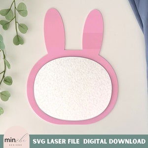 May include: Pink bunny shaped mirror with a round center. The mirror is blank and ready for personalization.