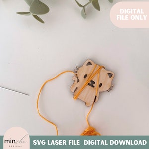 Puede incluir: Un porta hilos de madera con forma de gato con hilo amarillo enrollado alrededor. El porta hilos tiene una linda cara de dibujos animados con ojos, nariz y boca. El hilo está unido a una aguja.