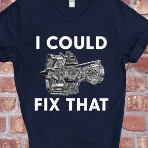 Può includere: Una maglietta blu navy con una grafica di un motore a reazione bianco e il testo "Potrei aggiustare questo".