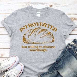May include: A gray t-shirt with the text "Introverted but willing to discuss sourdough." in brown lettering. A drawing of a loaf of bread is above the text.