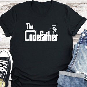 Op de afbeelding: Zwart T-shirt met witte tekst "The Codefather" met een kleine print van een circuitbord erboven.