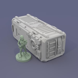 May include: A light gray, rectangular, futuristic storage container with detailed paneling and a small, green figurine of a soldier holding a weapon. The container has a series of vents and hatches.
