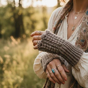 May include: A pair of brown fingerless gloves with a textured knit design. The gloves are worn with multiple silver rings, including one with a turquoise stone. The person is wearing a white blouse and a patterned scarf.
