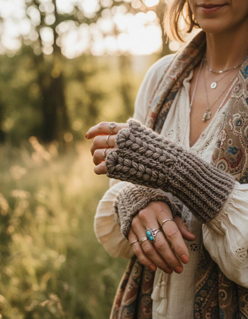 May include: A pair of brown fingerless gloves with a textured knit design. The gloves are worn with multiple silver rings, including one with a turquoise stone. The person is wearing a white blouse and a patterned scarf.