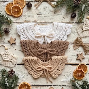 May include: Three crocheted collars in white, brown, and beige, each with a bow tie. The collars are arranged on a rustic wooden surface, surrounded by dried orange slices, pine cones, and star-shaped ornaments, evoking a cozy, handmade aesthetic.