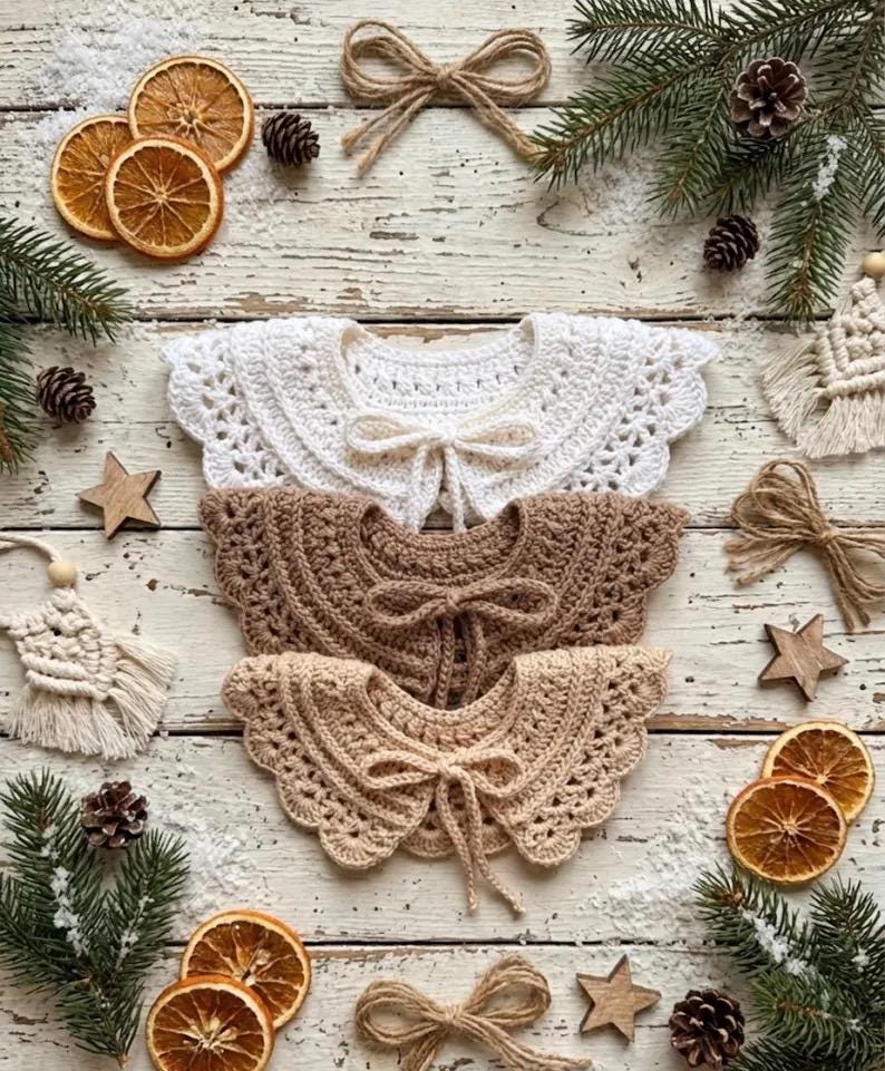May include: Three crocheted collars in white, brown, and beige, each with a bow tie. The collars are arranged on a rustic wooden surface, surrounded by dried orange slices, pine cones, and star-shaped ornaments, evoking a cozy, handmade aesthetic.