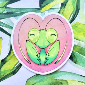 May include: A green praying mantis with large, round eyes and a happy expression is depicted inside a pink heart. The image is drawn in a cartoon style with watercolor-like textures.