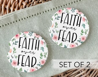 Peut inclure: Ensemble de deux dessous de verre ronds pour voiture avec un motif floral. Chaque dessous de verre porte l'inscription "Faith over Fear" en noir, entourée de roses roses et de feuilles vertes sur fond blanc.