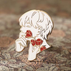 May include: A white enamel pin with a gold outline, featuring a side profile of a person holding red roses. The pin has a detailed design with a smooth finish, perfect for jackets, bags, or hats. The pin is a unique accessory.