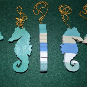 May include: Five seahorse ornaments with gold chains. Two seahorses are teal blue, two are white, blue, and beige, and one is a teal blue and white striped ornament.