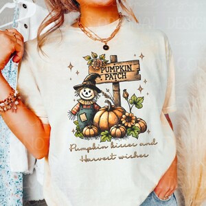 May include: A white t-shirt with a graphic of a scarecrow, pumpkins, and a sign that says "Pumpkin Patch". The text "Pumpkin kisses and harvest wishes" is printed below the graphic.