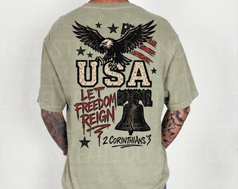 May include: Sage green t-shirt with a distressed graphic featuring a bald eagle, American flag, and the text "USA LET FREEDOM REIGN 2 CORINTHIANS 3". The design includes stars and a bell.
