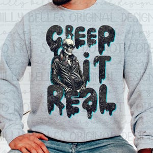May include: A gray sweatshirt with a black and white graphic of a skeleton wearing a leather jacket and sunglasses. The text "CREEP IT REAL" is printed in black with a blue outline.