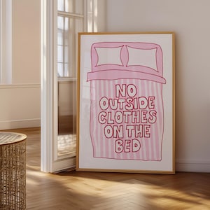 Può includere: Un poster a strisce rosa e bianche con un'illustrazione di un letto in stile cartone animato e il testo "NO OUTSIDE CLOTHES ON THE BED".