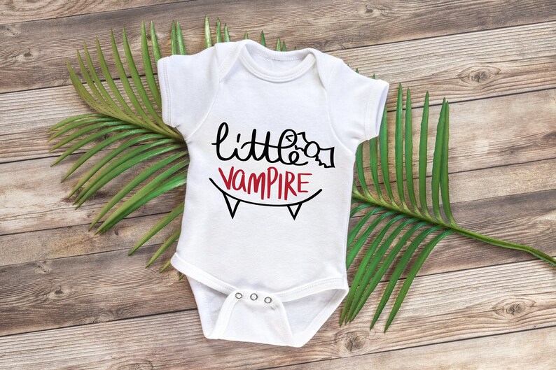 May include: White baby onesie with black and red text that reads "little vampire" with a black and white graphic of fangs.