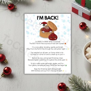 Op de afbeelding: Een rechthoekige witte kaart met een cartoon van een figuur met een kerstmuts in een bamboe stoommandje, naast een rode glinsterende dumpling. De tekst luidt: I'M BACK! I'm BACK! I'm BACK! What a surprise! The BEST North Pole surprise arrived with a prize!