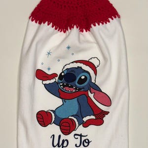 Puede incluir: Toalla de cocina blanca con parte superior de ganchillo roja y cierre de bot&oacute;n. Presenta un personaje de dibujos animados azul con gorro y bufanda de Pap&aacute; Noel, con el texto "Up To SNOW GOOD" en rojo.