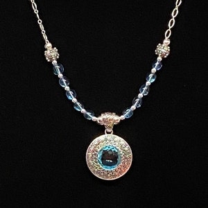 Handmade necklace features very pretty sterling silver pendant set with a faceted synthetic blue topaz and accented with glass and sterling