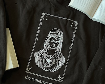 May include: A black sweatshirt with a white graphic design of a woman's bust with a celestial body inside. The text "the romance reader" is printed below the graphic.