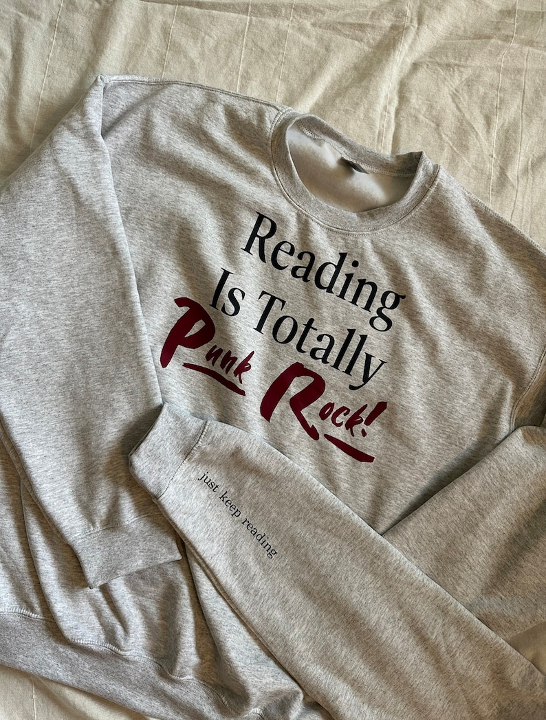 May include: Gray sweatshirt with the text "Reading is Totally Punk Rock!" in black and red lettering. The text "Just keep reading" is printed in black on the sleeve.