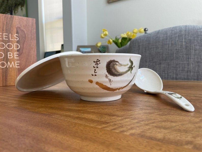 May include: White ceramic bowl with a lid and a matching spoon. The bowl has a gold and green design with Japanese characters.