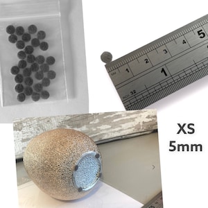 May include: A close-up of a small, round, grey felt pad measuring 5mm in diameter. The pad is shown next to a ruler for scale. The pad is packaged in a clear plastic bag with other similar pads.