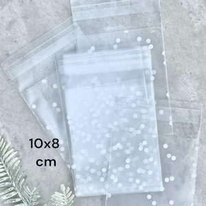 May include: Several clear cellophane bags with white polka dots. The bags are 10 x 8 cm in size. The bags are stacked on top of each other. The bags are sealed at the top.